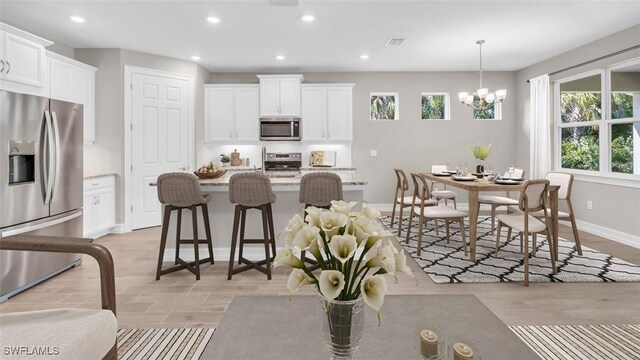 kitchen with white cabinetry, an island with sink, decorative light fixtures, and appliances with stainless steel finishes