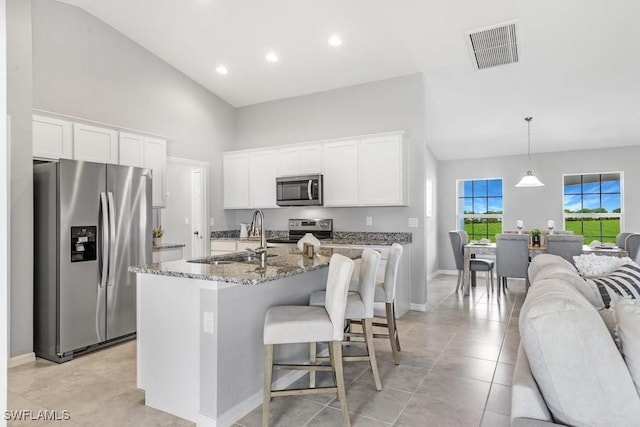 kitchen featuring white cabinetry, high vaulted ceiling, hanging light fixtures, a center island with sink, and stainless steel appliances