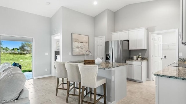 kitchen with white cabinets, an island with sink, stainless steel fridge, and stone counters