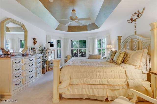 carpeted bedroom featuring ceiling fan and a tray ceiling