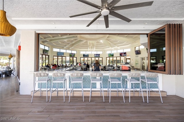 bar with beam ceiling, ceiling fan, wood-type flooring, and a textured ceiling