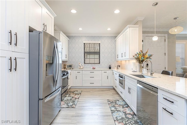 kitchen with sink, hanging light fixtures, stainless steel appliances, white cabinets, and ornamental molding