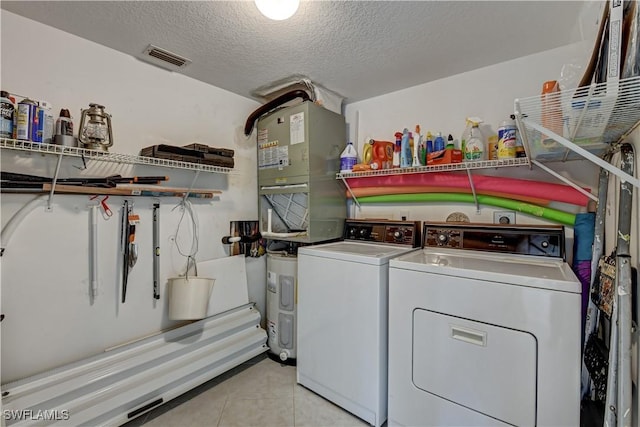 clothes washing area with washing machine and dryer, light tile patterned floors, and a textured ceiling