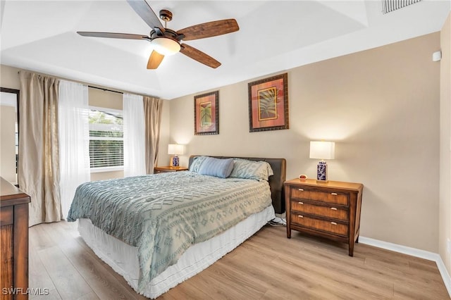 bedroom featuring ceiling fan, light hardwood / wood-style floors, and a raised ceiling