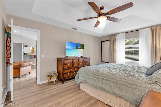 bedroom featuring a raised ceiling, ceiling fan, and light wood-type flooring