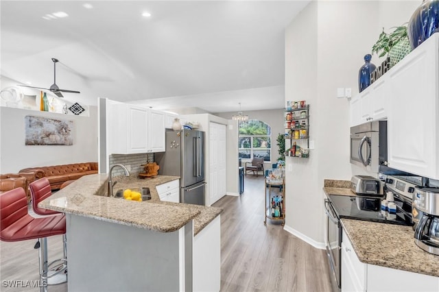 kitchen with kitchen peninsula, a kitchen bar, stainless steel appliances, sink, and white cabinetry