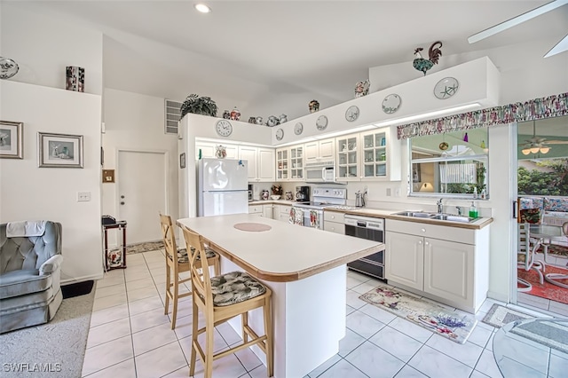 kitchen featuring white cabinetry, sink, white appliances, a breakfast bar area, and light tile patterned flooring