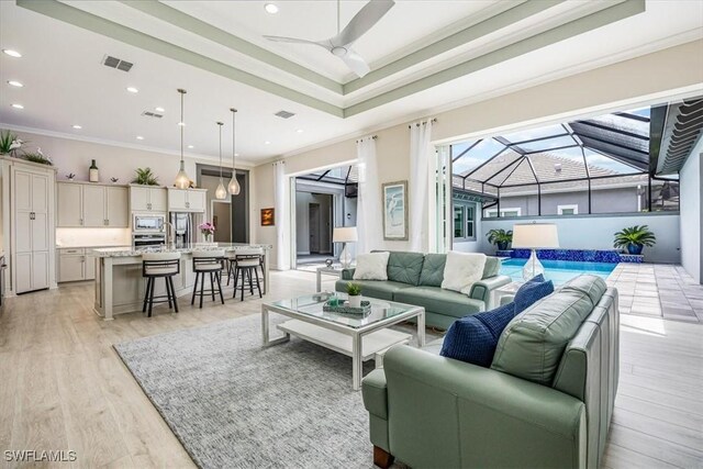 living room with a raised ceiling, ceiling fan, light wood-type flooring, and ornamental molding