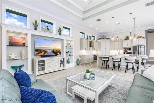 living room featuring light hardwood / wood-style floors, sink, a towering ceiling, and crown molding