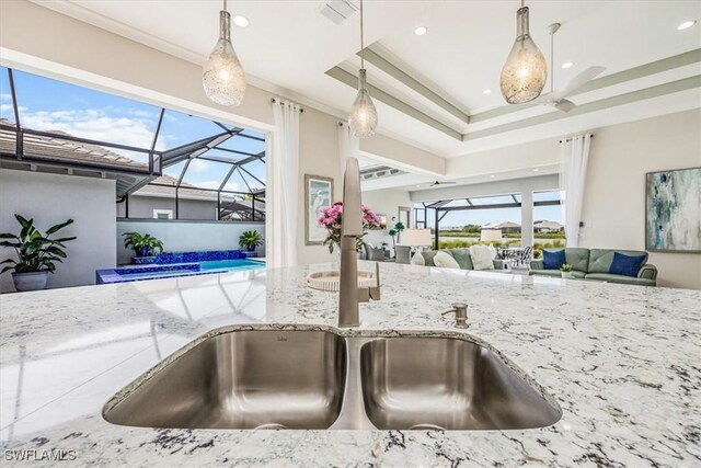 kitchen with a tray ceiling, light stone counters, a healthy amount of sunlight, and decorative light fixtures