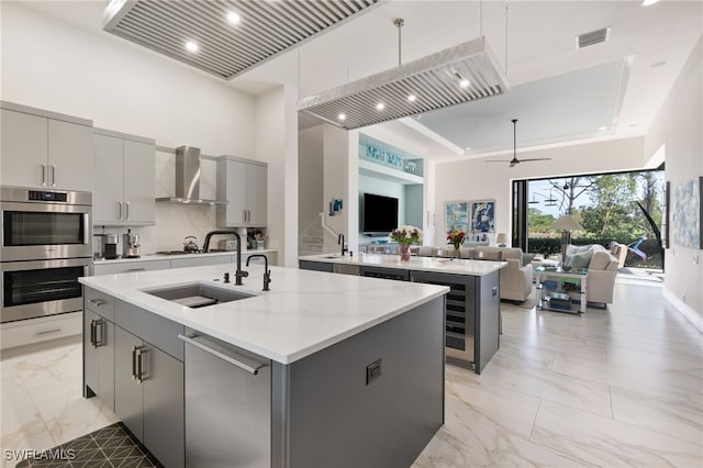 kitchen featuring a kitchen island with sink, wall chimney range hood, gray cabinets, and stainless steel appliances