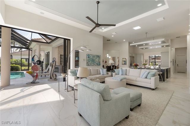 living room with ceiling fan, a high ceiling, and a tray ceiling