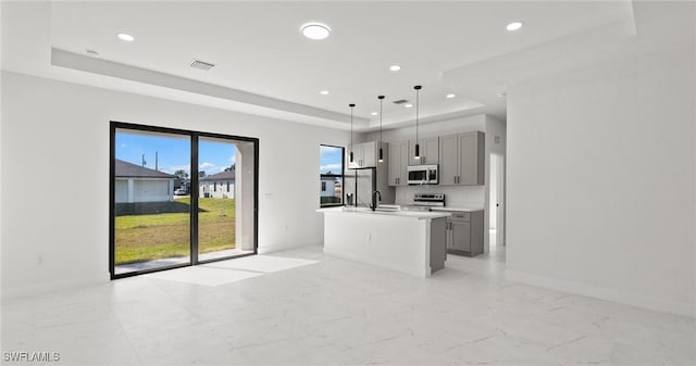 kitchen featuring gray cabinetry, a center island with sink, appliances with stainless steel finishes, a tray ceiling, and decorative light fixtures