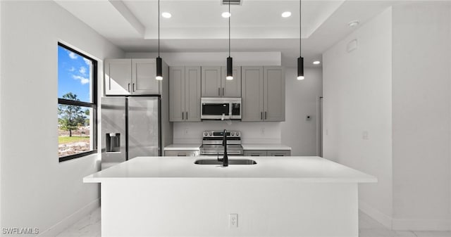 kitchen with a kitchen island with sink, gray cabinets, appliances with stainless steel finishes, a tray ceiling, and decorative light fixtures