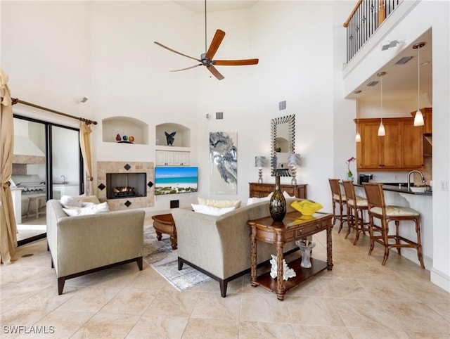 living room with ceiling fan, built in features, a towering ceiling, and a tiled fireplace