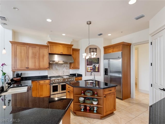 kitchen with tasteful backsplash, premium appliances, sink, decorative light fixtures, and a center island with sink