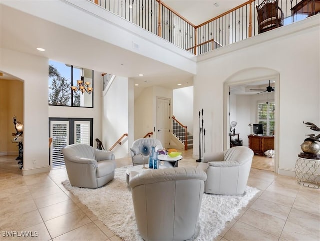 living room with a high ceiling, ceiling fan with notable chandelier, and light tile patterned flooring