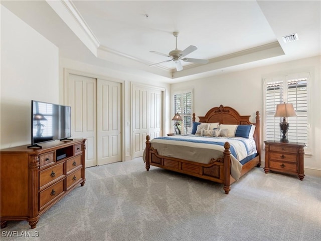 carpeted bedroom with a raised ceiling, ceiling fan, and two closets