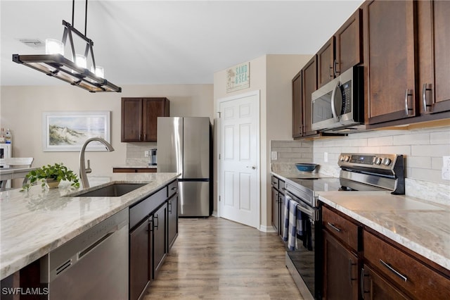 kitchen featuring appliances with stainless steel finishes, light stone counters, dark brown cabinets, sink, and pendant lighting