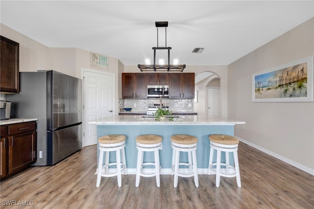 kitchen with a center island with sink, dark brown cabinets, decorative light fixtures, and appliances with stainless steel finishes