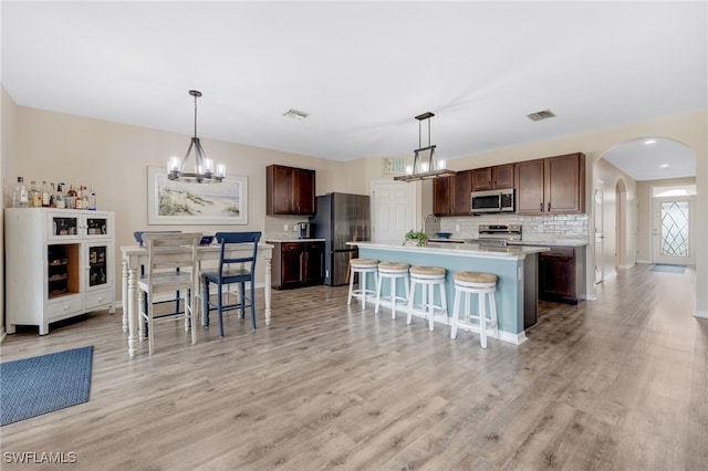 kitchen with a center island with sink, decorative light fixtures, a breakfast bar, and appliances with stainless steel finishes