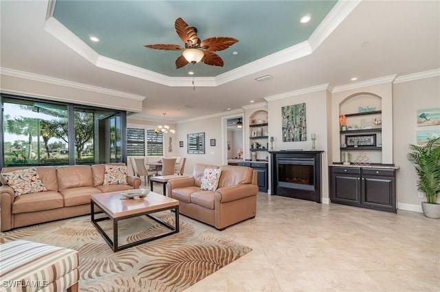 living room with ceiling fan with notable chandelier, a raised ceiling, built in features, and crown molding