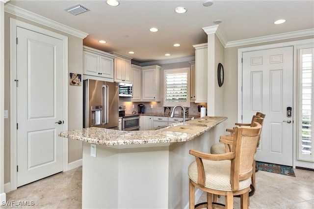 kitchen featuring kitchen peninsula, appliances with stainless steel finishes, light stone counters, sink, and a breakfast bar area