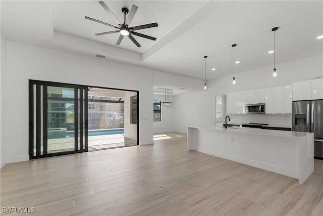 kitchen with white cabinets, hanging light fixtures, ceiling fan, an island with sink, and appliances with stainless steel finishes