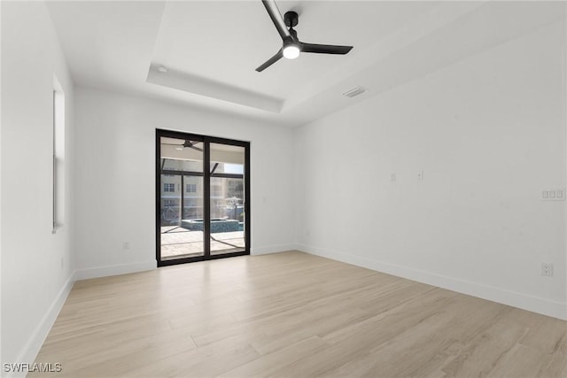 spare room with a raised ceiling, ceiling fan, and light hardwood / wood-style floors