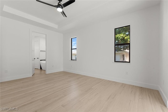 spare room with a tray ceiling, ceiling fan, and light hardwood / wood-style floors