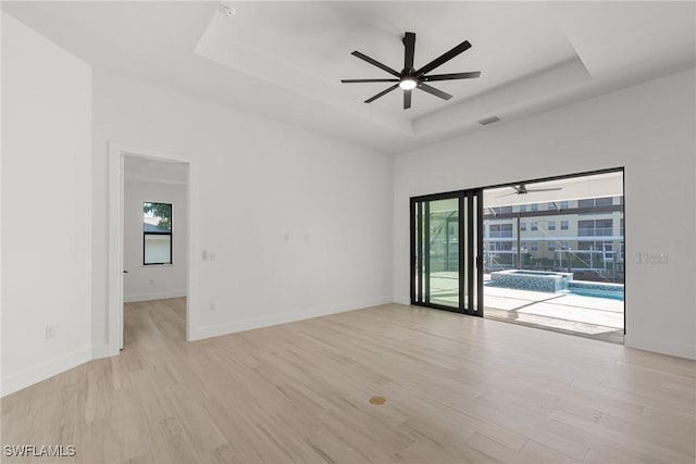 empty room with light hardwood / wood-style floors, a raised ceiling, and ceiling fan