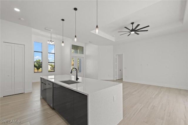 kitchen with a large island, sink, ceiling fan, a raised ceiling, and pendant lighting