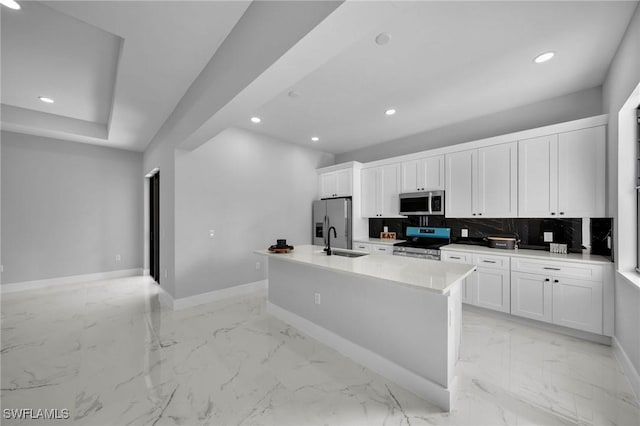 kitchen featuring sink, stainless steel appliances, backsplash, a center island with sink, and white cabinets