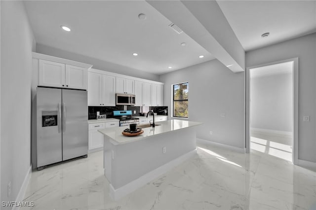 kitchen with backsplash, stainless steel appliances, sink, white cabinets, and an island with sink