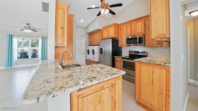 kitchen featuring kitchen peninsula, washer and clothes dryer, lofted ceiling, appliances with stainless steel finishes, and sink