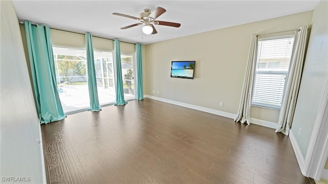 empty room featuring ceiling fan, a wealth of natural light, and dark wood-type flooring