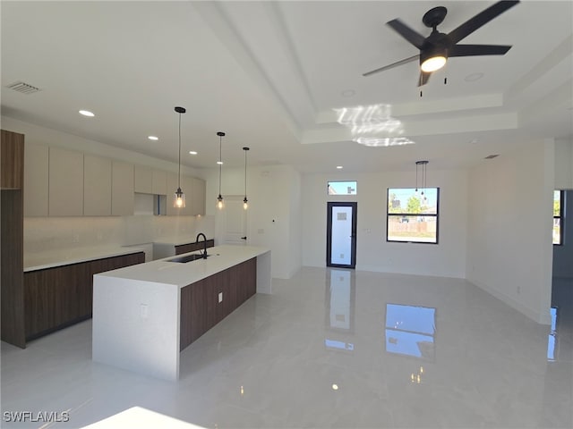 kitchen with sink, decorative light fixtures, an island with sink, and a raised ceiling