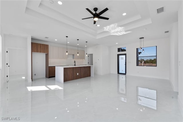 kitchen featuring sink, hanging light fixtures, a kitchen island with sink, ceiling fan, and a raised ceiling