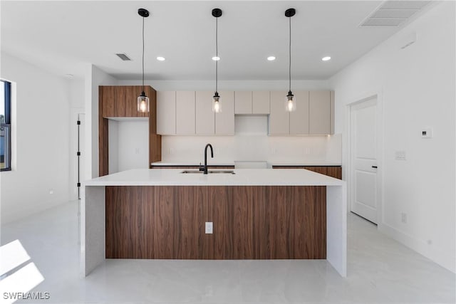 kitchen featuring pendant lighting, an island with sink, sink, and white cabinets