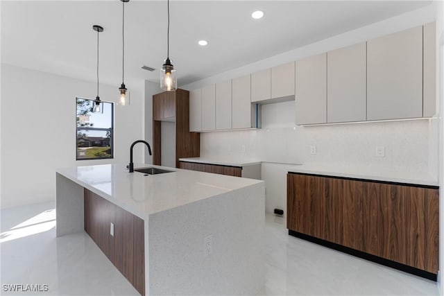 kitchen with sink, tasteful backsplash, white cabinets, a center island with sink, and decorative light fixtures