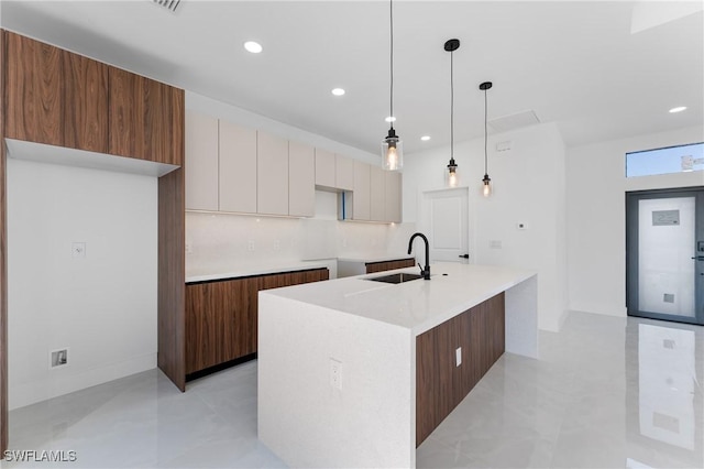 kitchen with decorative light fixtures, white cabinetry, sink, decorative backsplash, and a center island with sink