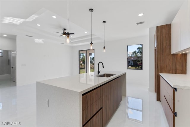 kitchen with white cabinetry, sink, hanging light fixtures, a tray ceiling, and a spacious island