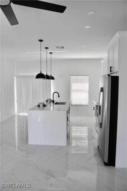 kitchen with freestanding refrigerator, marble finish floor, a kitchen island with sink, white cabinetry, and a sink