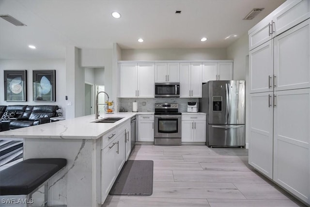 kitchen featuring sink, white cabinetry, appliances with stainless steel finishes, kitchen peninsula, and light stone countertops