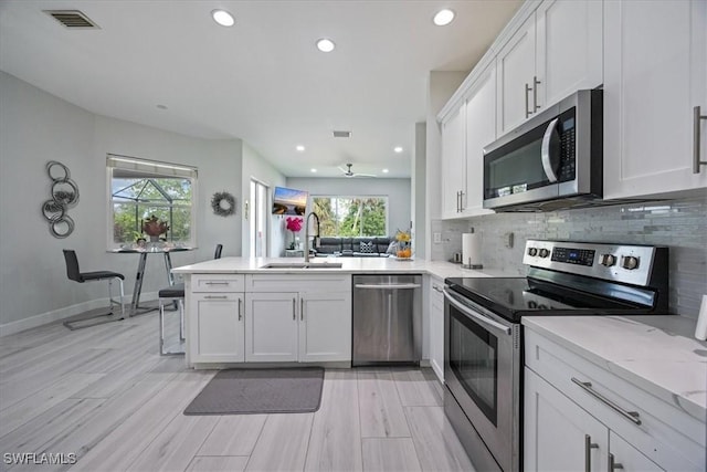 kitchen with sink, kitchen peninsula, stainless steel appliances, decorative backsplash, and white cabinets