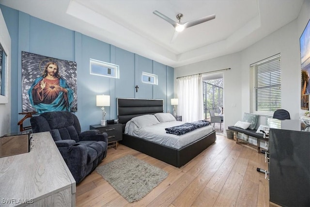 bedroom featuring hardwood / wood-style flooring, access to exterior, ceiling fan, and a tray ceiling