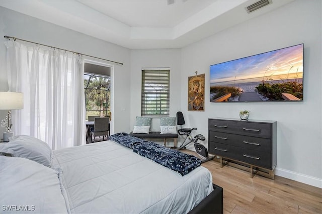 bedroom featuring access to exterior, wood-type flooring, and a raised ceiling