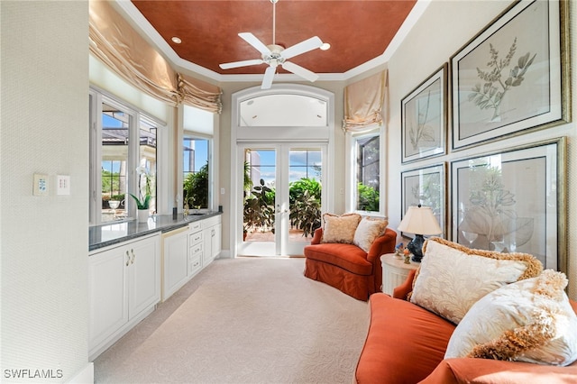 living area with ceiling fan, crown molding, light carpet, and a wealth of natural light