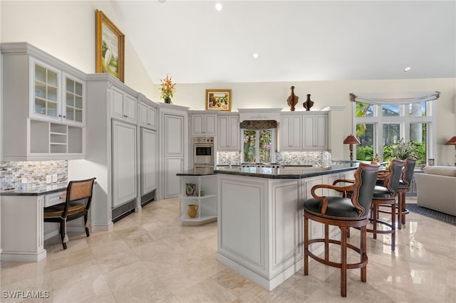 kitchen with decorative backsplash, a breakfast bar, a center island, gray cabinets, and lofted ceiling