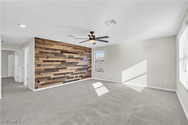 spare room featuring light colored carpet, ceiling fan, and wooden walls